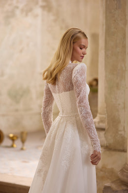 Ivory wedding dress with a sheer lace back, long lace sleeves, fitted waist, and flowing skirt