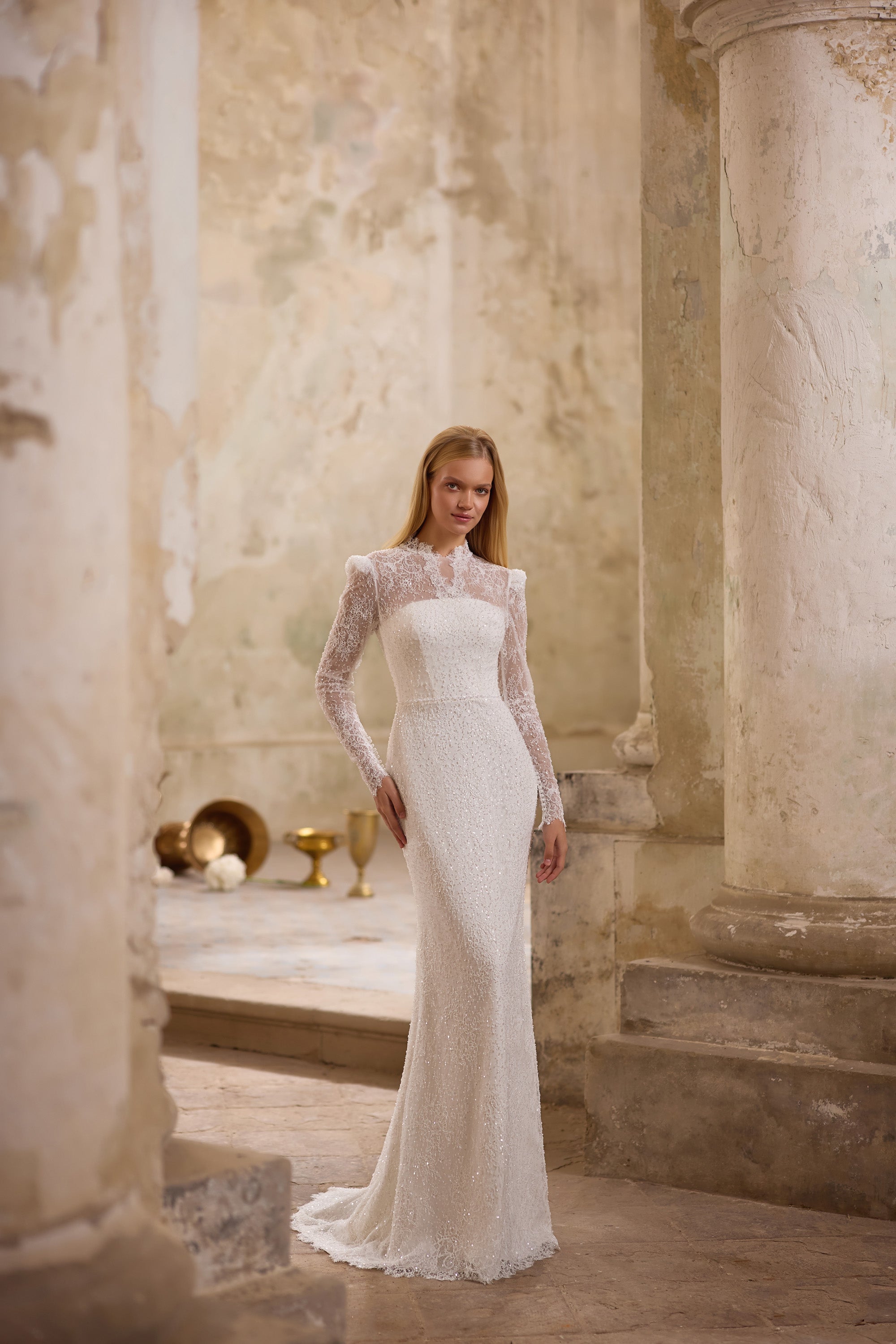 Ivory mermaid wedding dress with a high sheer neckline, long lace sleeves, sparkling embellishment, and train
