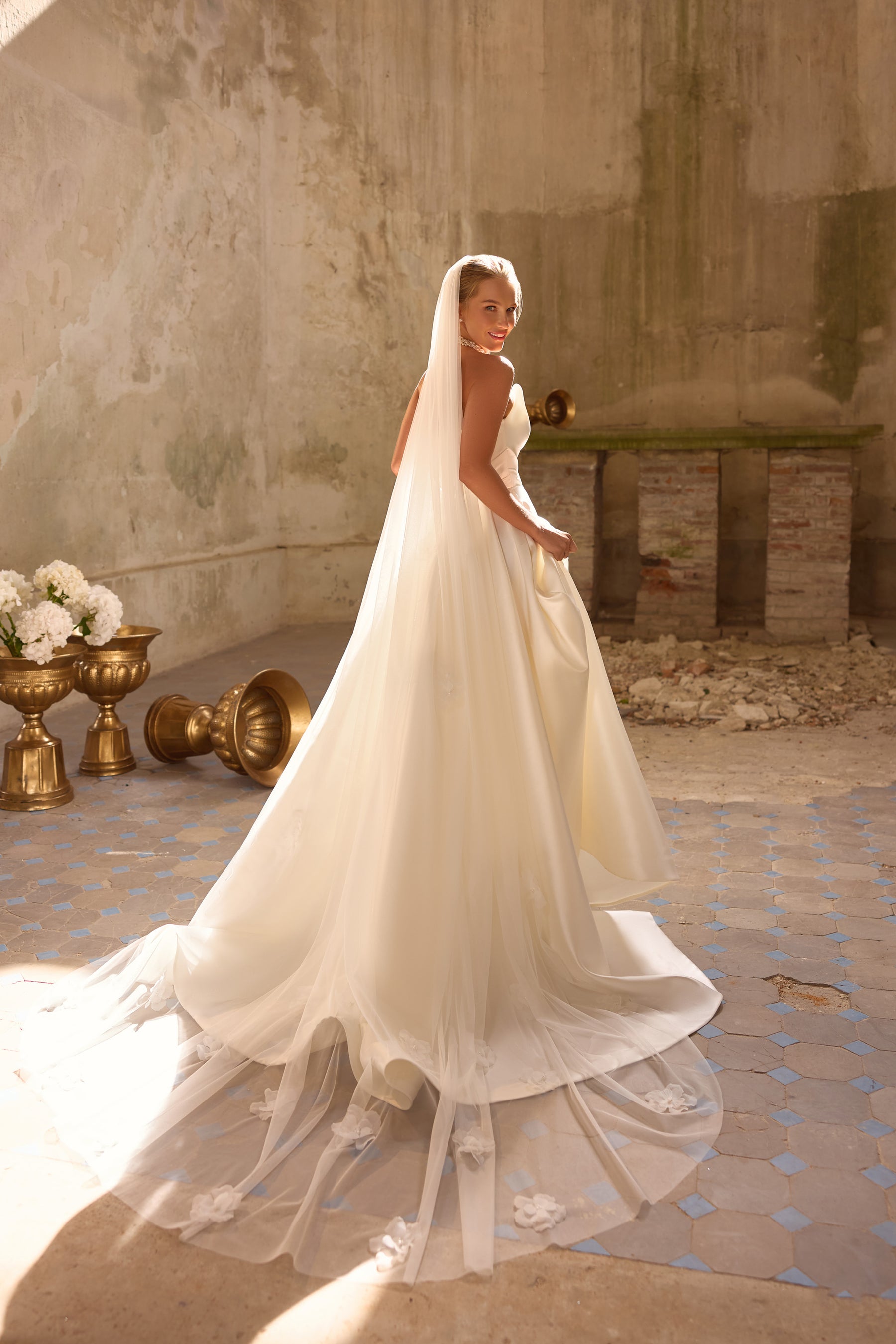 Ivory wedding dress with a flowing overskirt, sheer floral-trimmed hem, and extended train