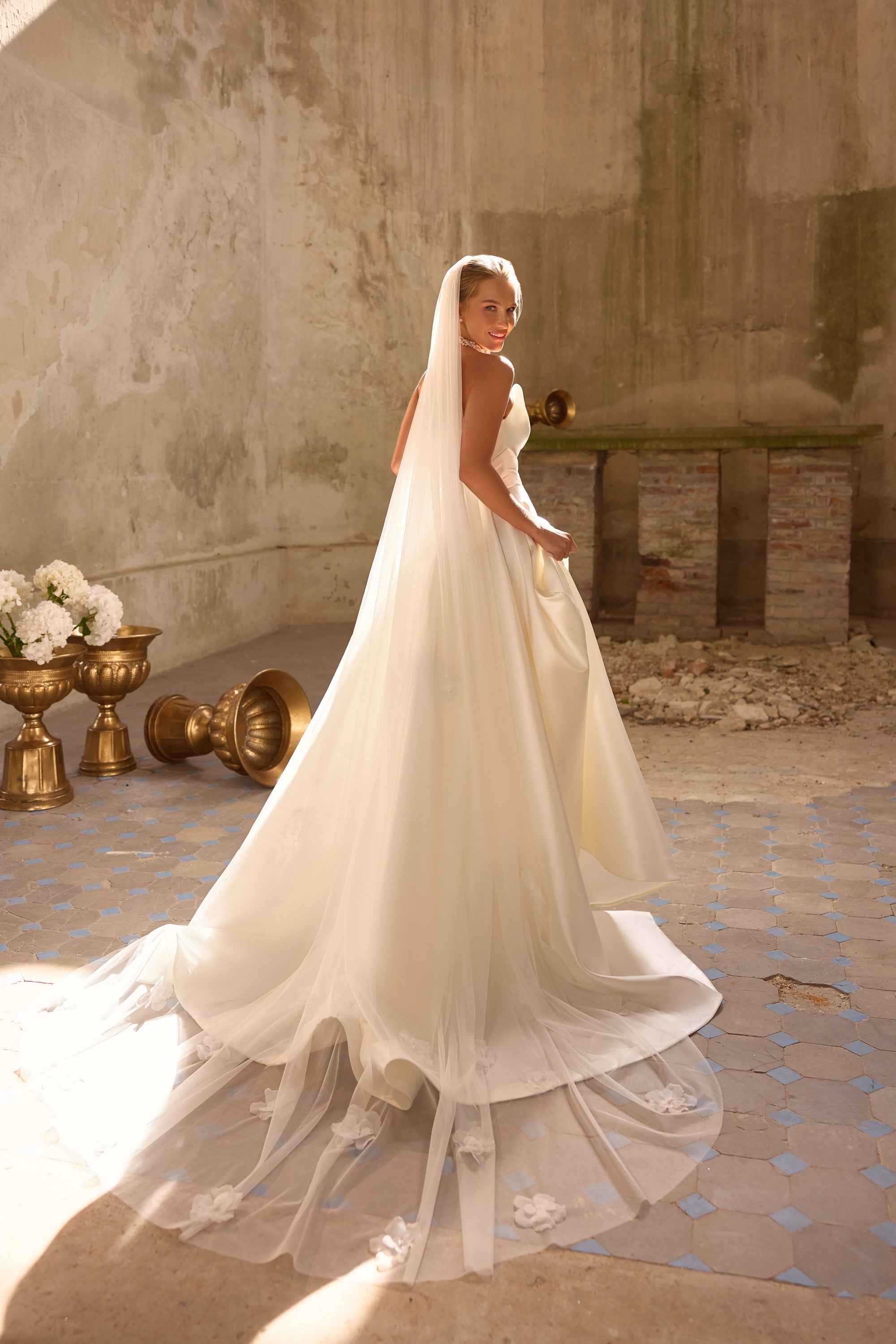 Ivory wedding dress with a flowing overskirt, sheer floral-trimmed hem, and extended train