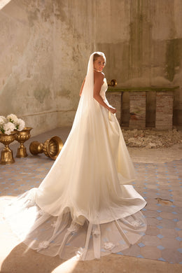 Ivory wedding dress with a flowing overskirt, sheer floral-trimmed hem, and extended train