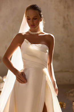 Close-up of an ivory wedding dress with a draped asymmetric neckline, fitted bodice, and thigh slit