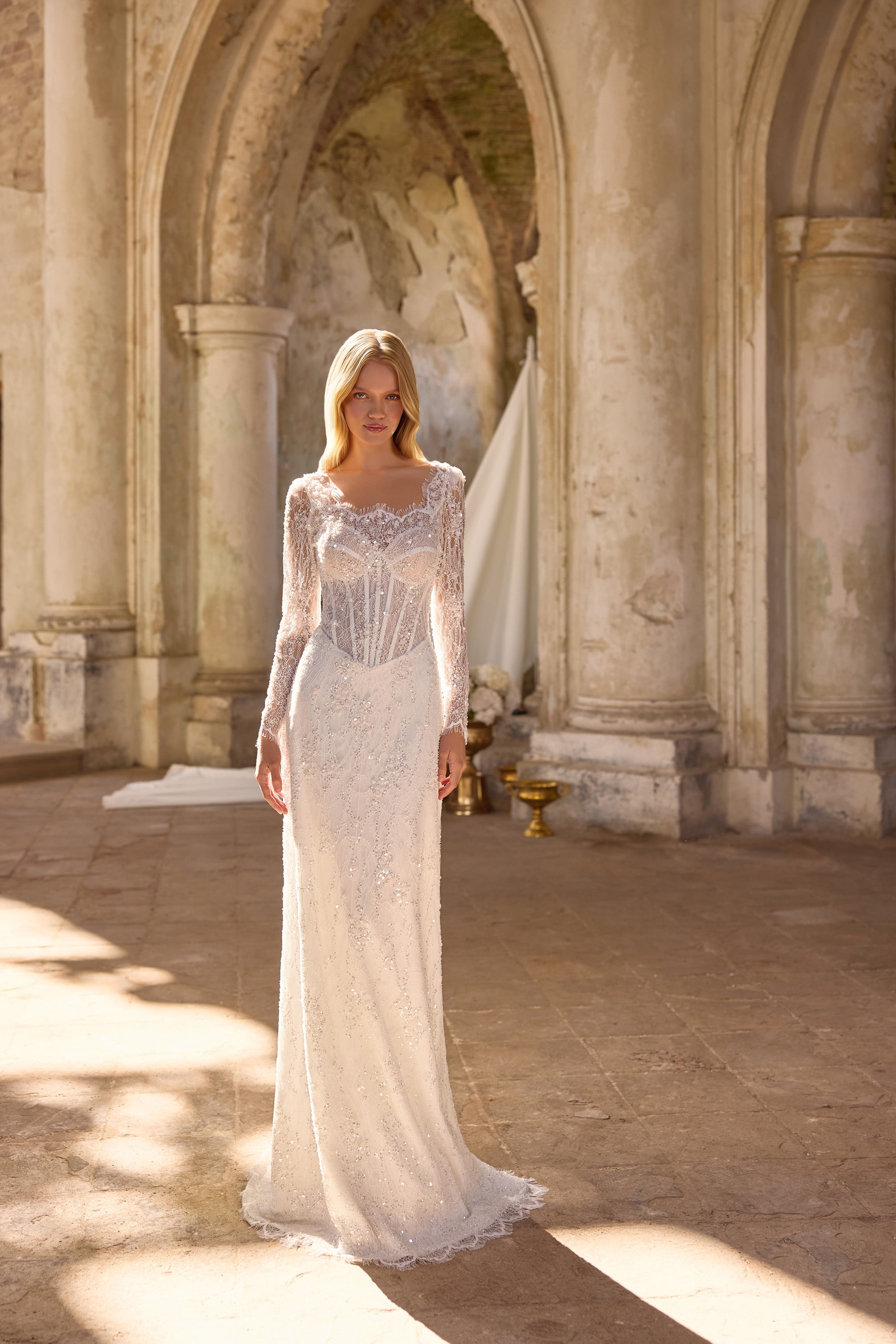 Full-length ivory wedding dress featuring a fitted mermaid silhouette, sheer lace sleeves, and a long train