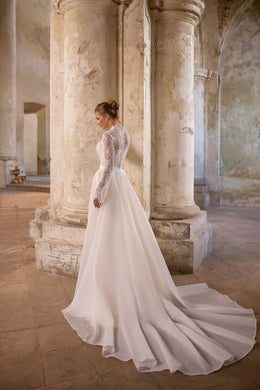 Ivory wedding dress with long lace sleeves, a fitted bodice, and flowing detachable overskirt trailing into a train