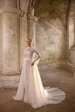 Ivory wedding dress with a high lace neckline, long sleeves, fitted lace center panel, and detachable overskirt