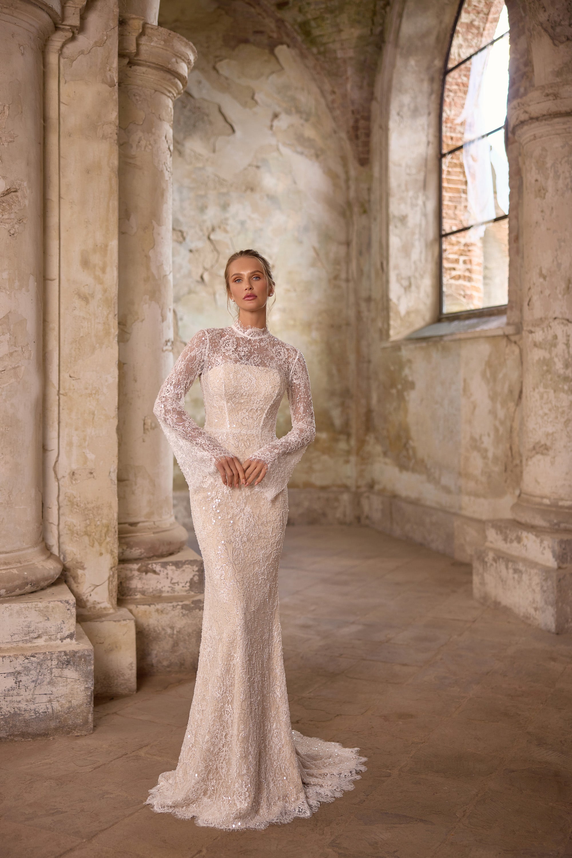 Fitted ivory wedding dress covered in lace and shimmering beadwork, with a high neckline, long sleeves, and train