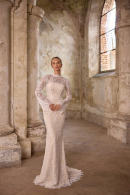Fitted ivory wedding dress covered in lace and shimmering beadwork, with a high neckline, long sleeves, and train