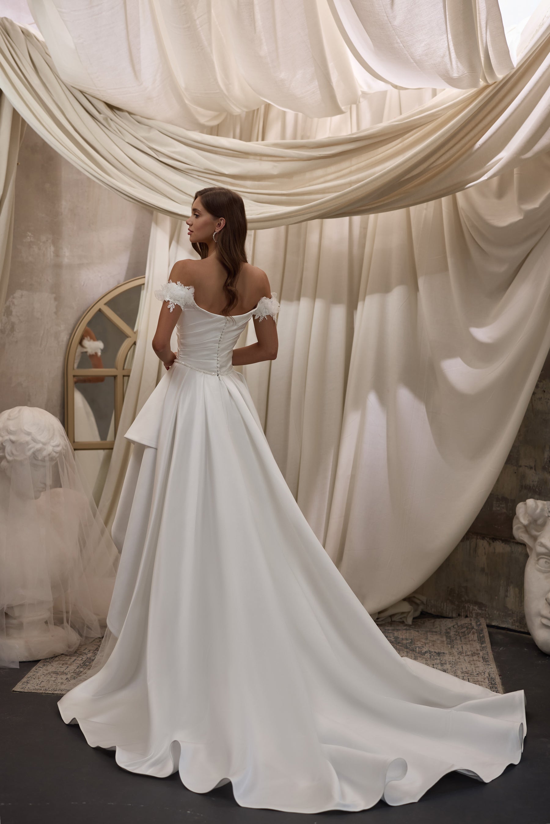 Back view of an ivory wedding dress with off-the-shoulder floral appliqués, fitted waist, and flowing train