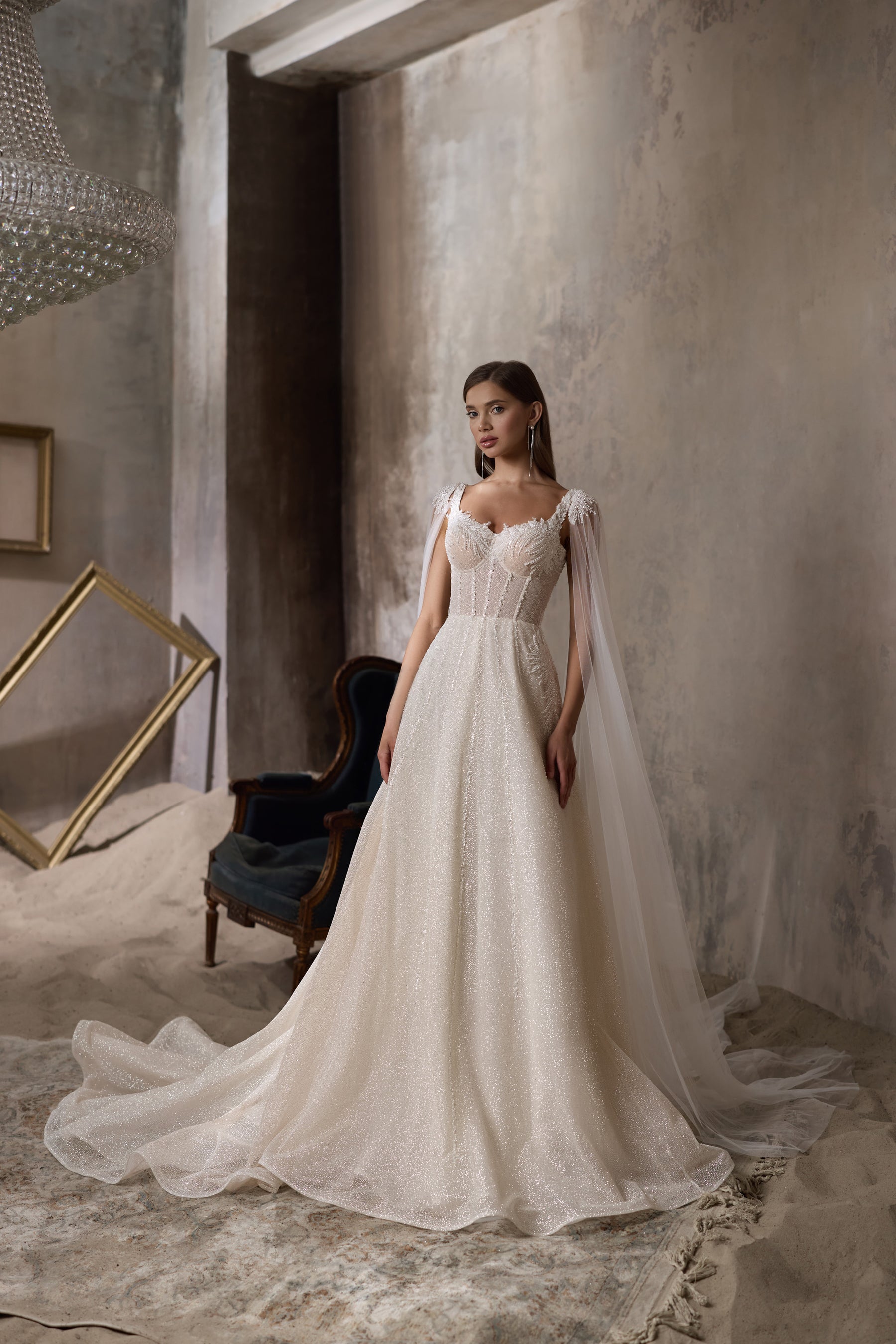 Ivory A-line wedding dress with a sparkling beaded bodice, sheer cape sleeves, and sweeping train