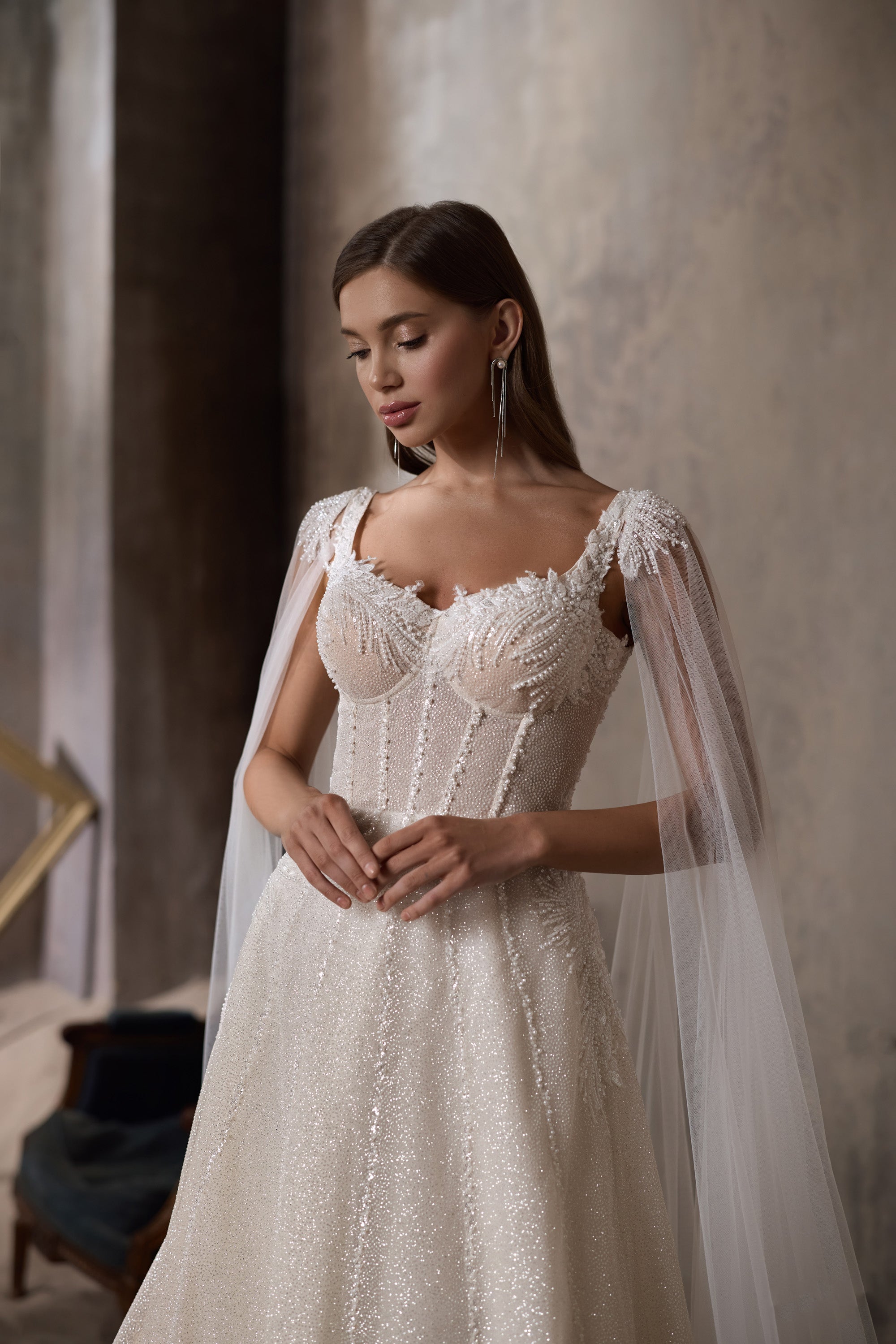 Ivory A-line wedding dress with a beaded sweetheart neckline, sheer cape sleeves, and sparkling bodice