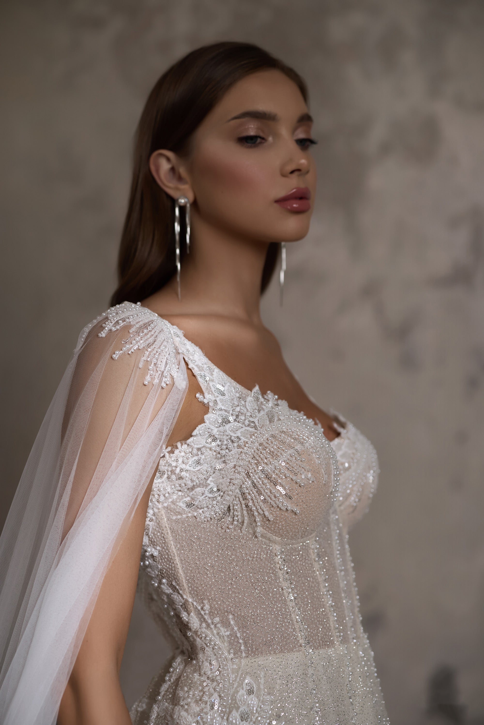 Close-up of floral beadwork and a sheer draped cape sleeve on an ivory wedding dress