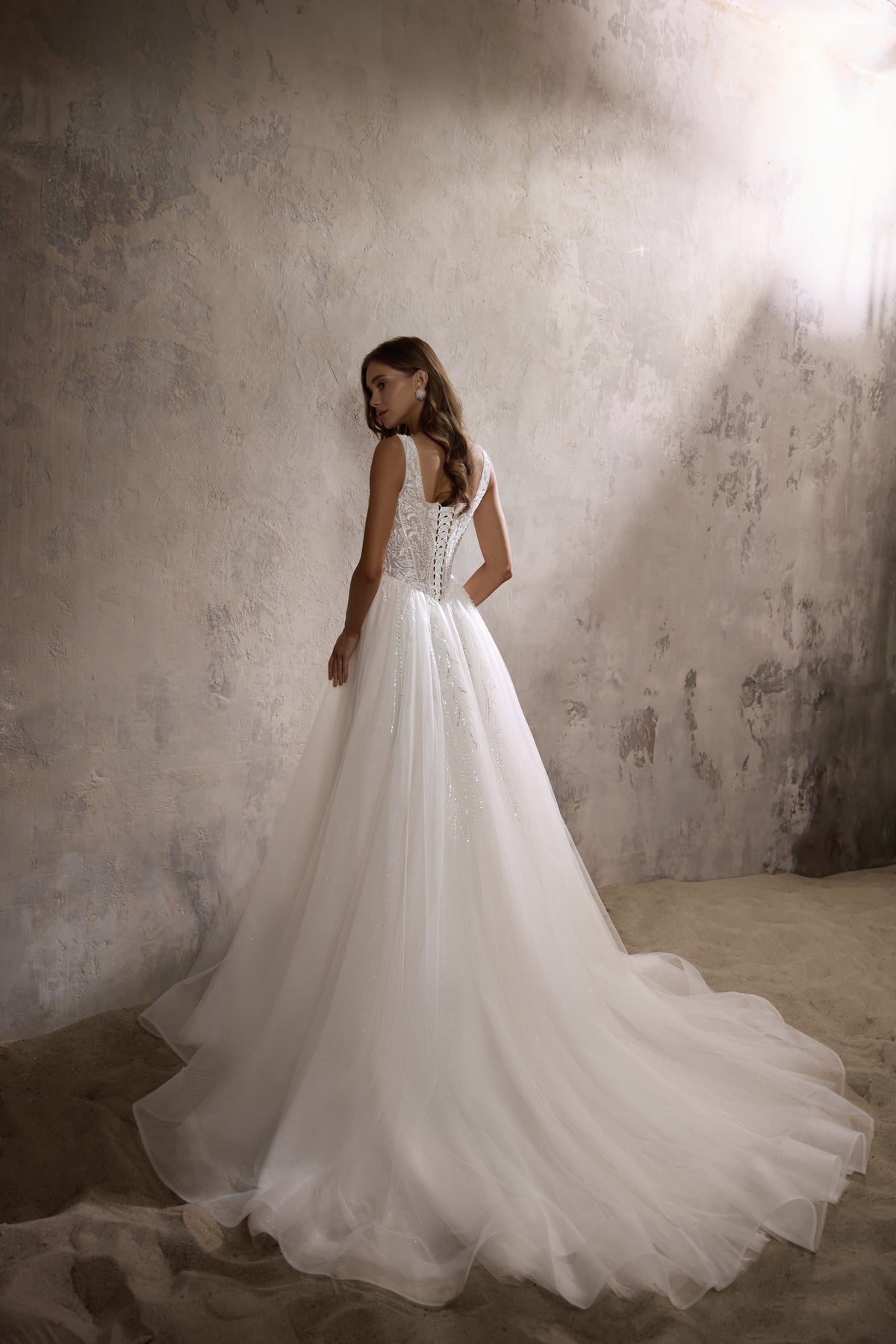 Rear three-quarter view of an ivory wedding dress with a beaded back, full skirt, and long train