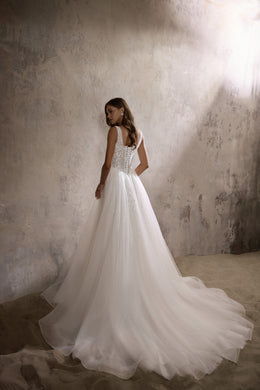 Rear three-quarter view of an ivory wedding dress with a beaded back, full skirt, and long train