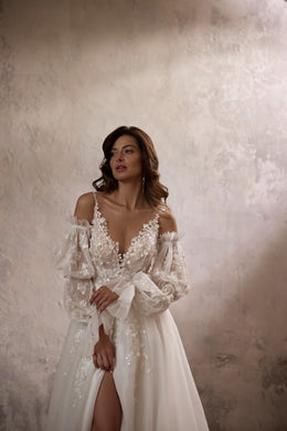 Close-up of an ivory wedding dress with floral lace appliqués, V-neckline, sheer sleeves, and waist bow