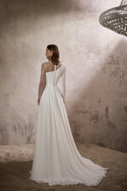 Back of an ivory wedding dress with a sheer sequined sleeve, defined waist, flowing skirt, and long train