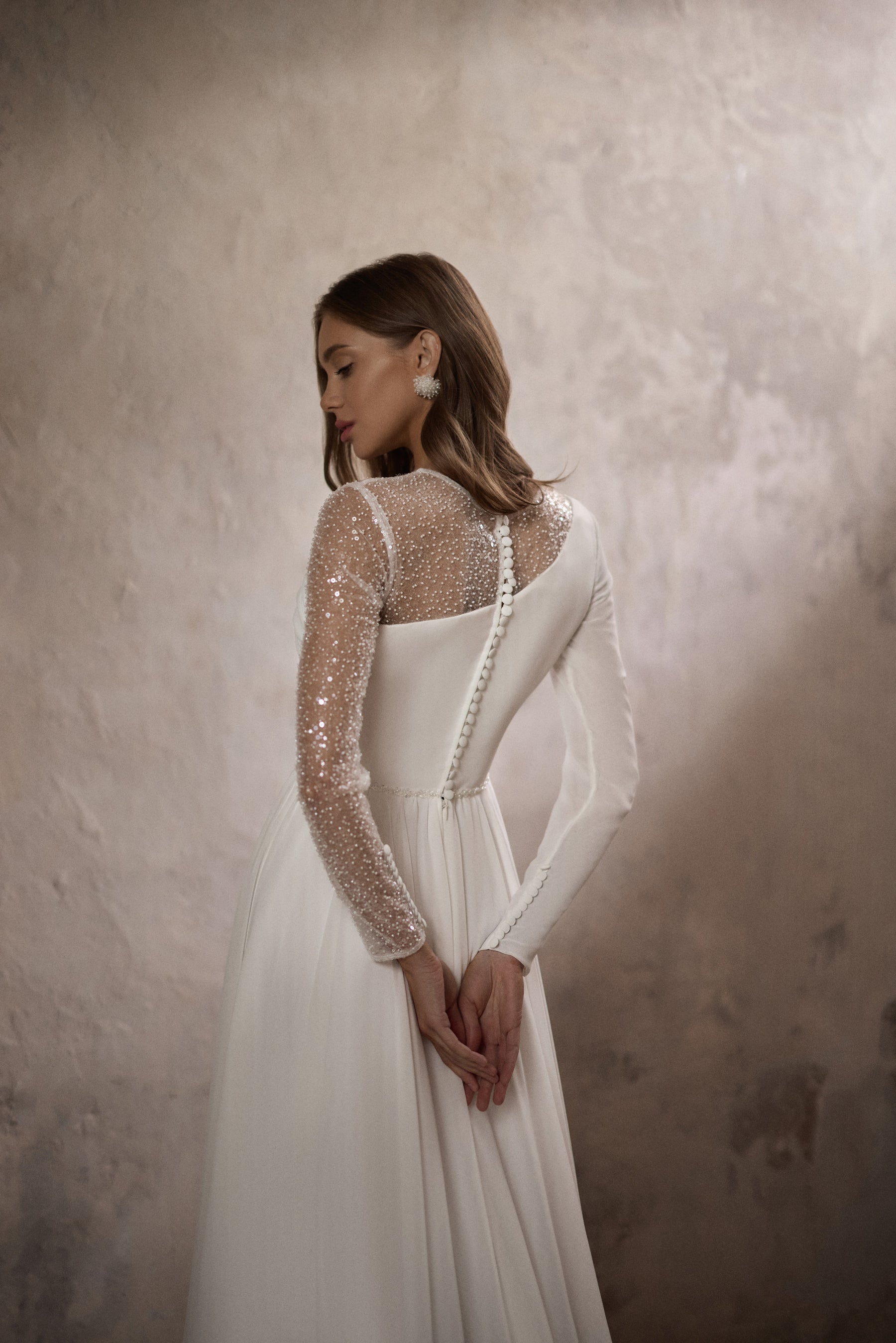 Close-up of the ivory wedding dress back with a sheer beaded sleeve and covered buttons