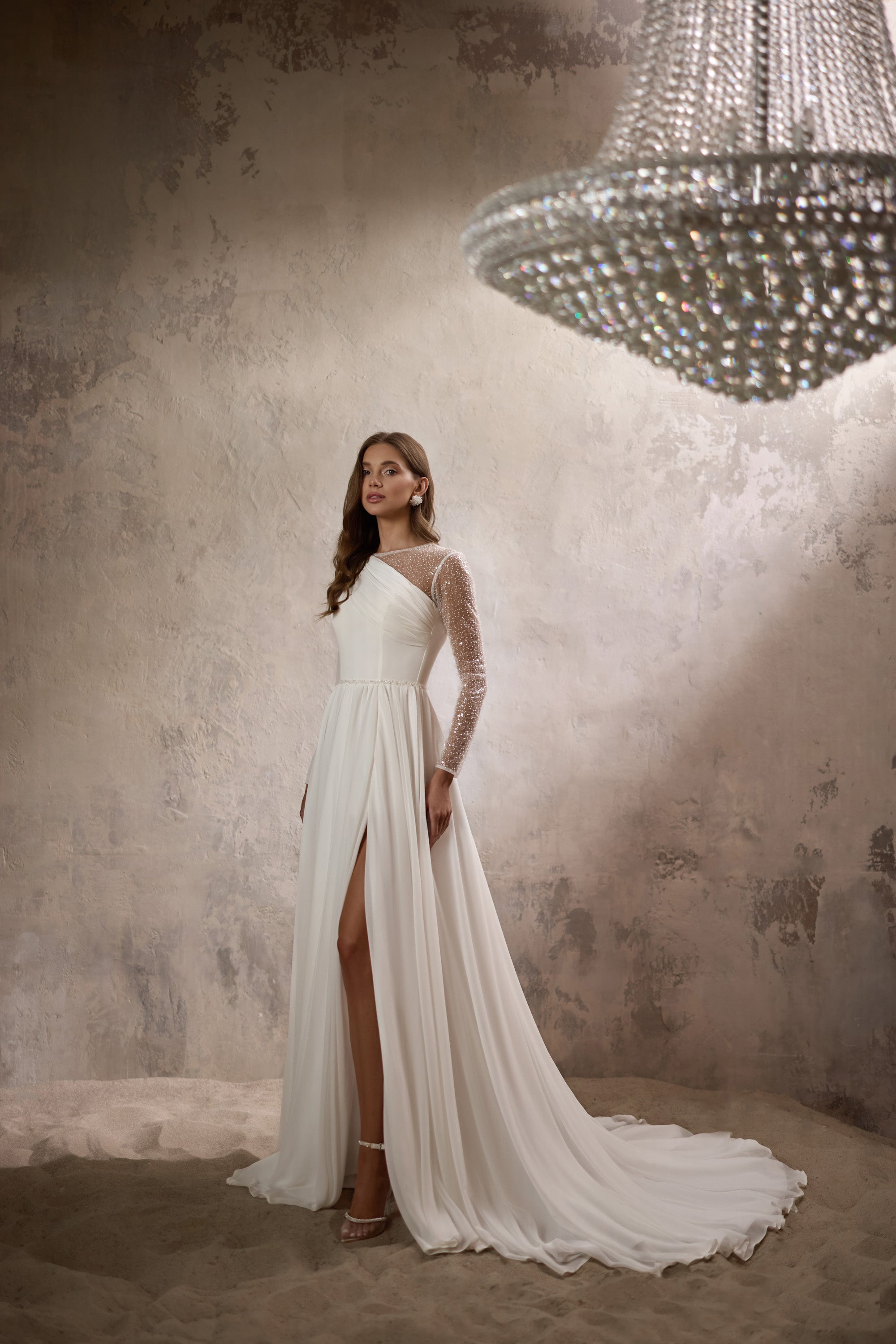 Ivory A-line wedding dress with an asymmetric neckline, glittering sheer sleeve, front slit, and long train