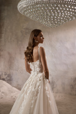 Ivory wedding dress with a low embellished back, thin straps, floral appliqués, and a flowing train