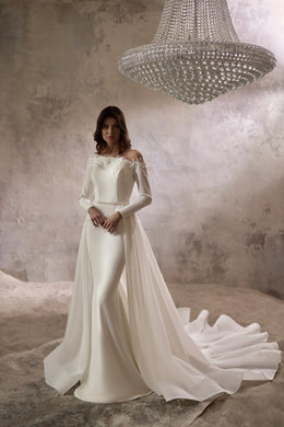 Ivory wedding dress with an off-the-shoulder lace neckline, long sleeves, fitted skirt, and flowing overskirt