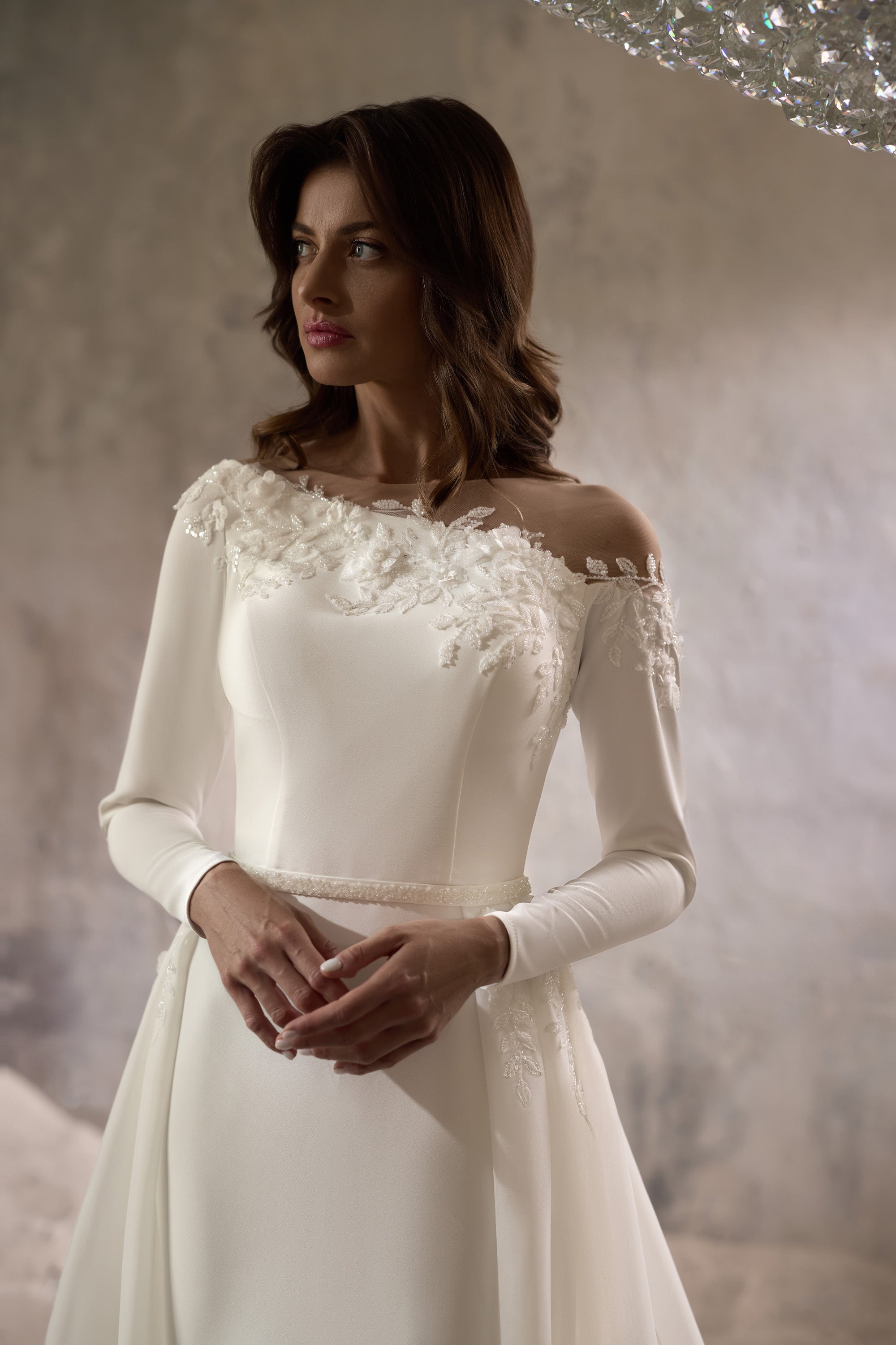Close-up of an ivory wedding dress with floral lace appliqués at the off-the-shoulder neckline and long sleeves