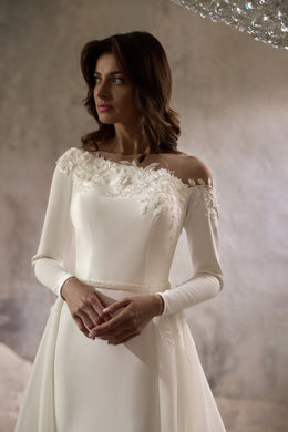 Close-up of an ivory wedding dress with floral lace appliqués at the off-the-shoulder neckline and long sleeves