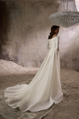 Three-quarter back view of an ivory wedding dress with a covered lace-trimmed back and long, flowing train