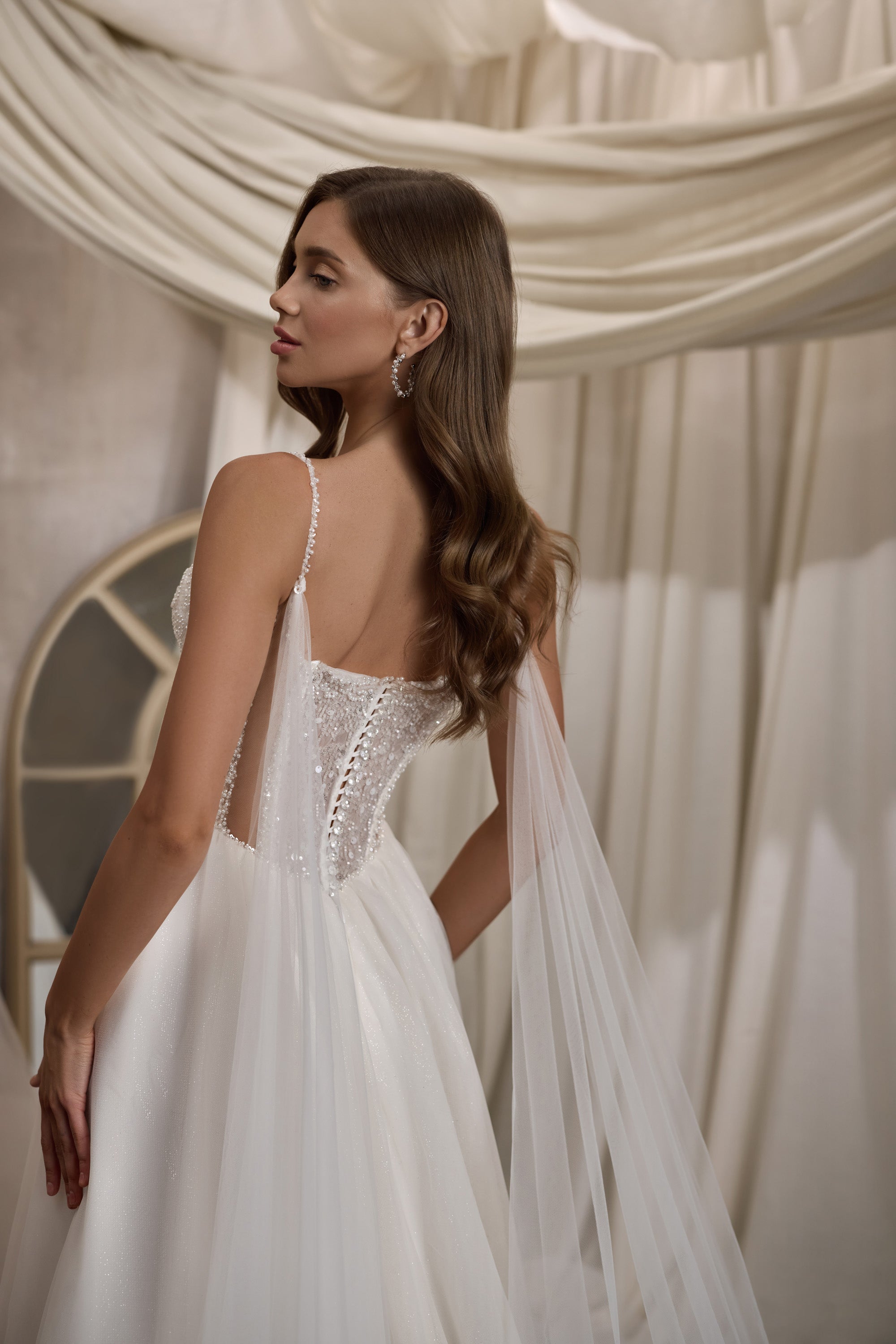 Close-up of the embellished open back and sheer cape on an ivory wedding dress