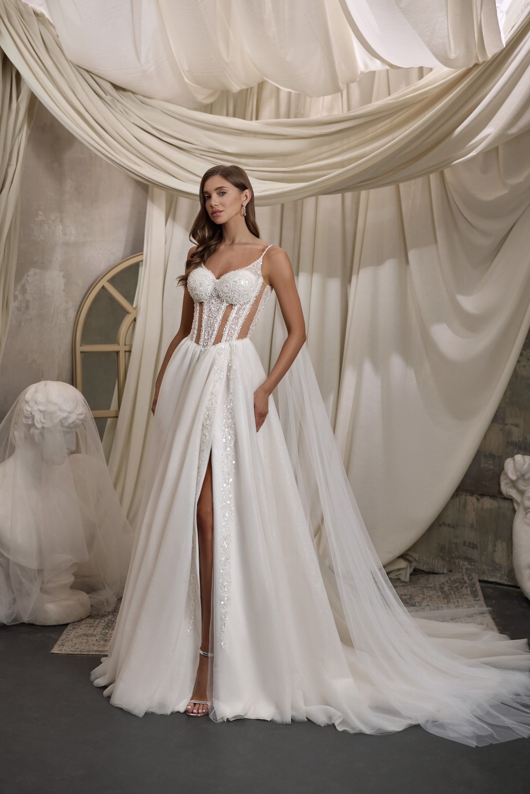 Ivory A-line wedding dress with a beaded corset bodice, thigh-high slit, and flowing sheer cape