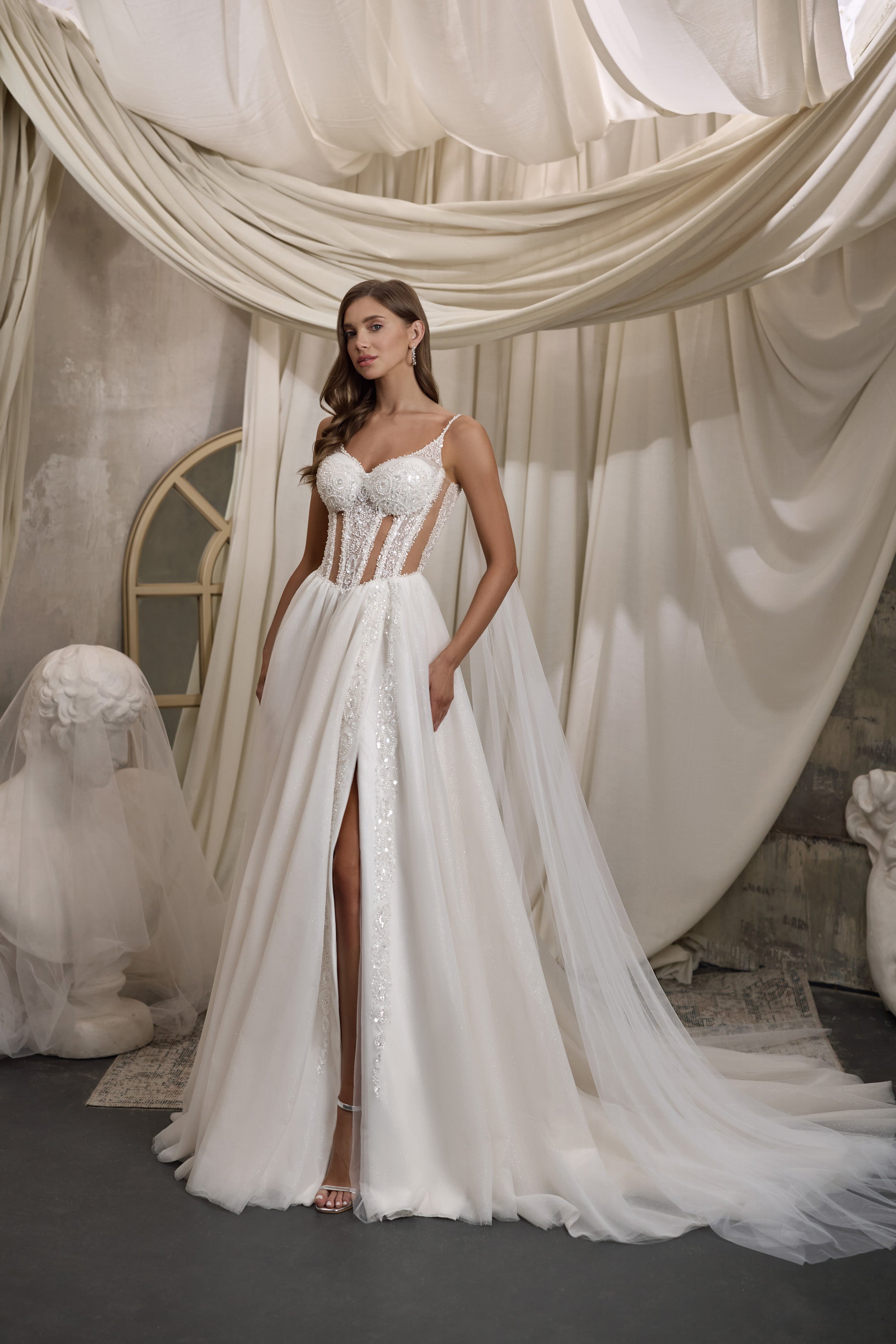 Ivory A-line wedding dress with a beaded corset bodice, thigh-high slit, and flowing sheer cape