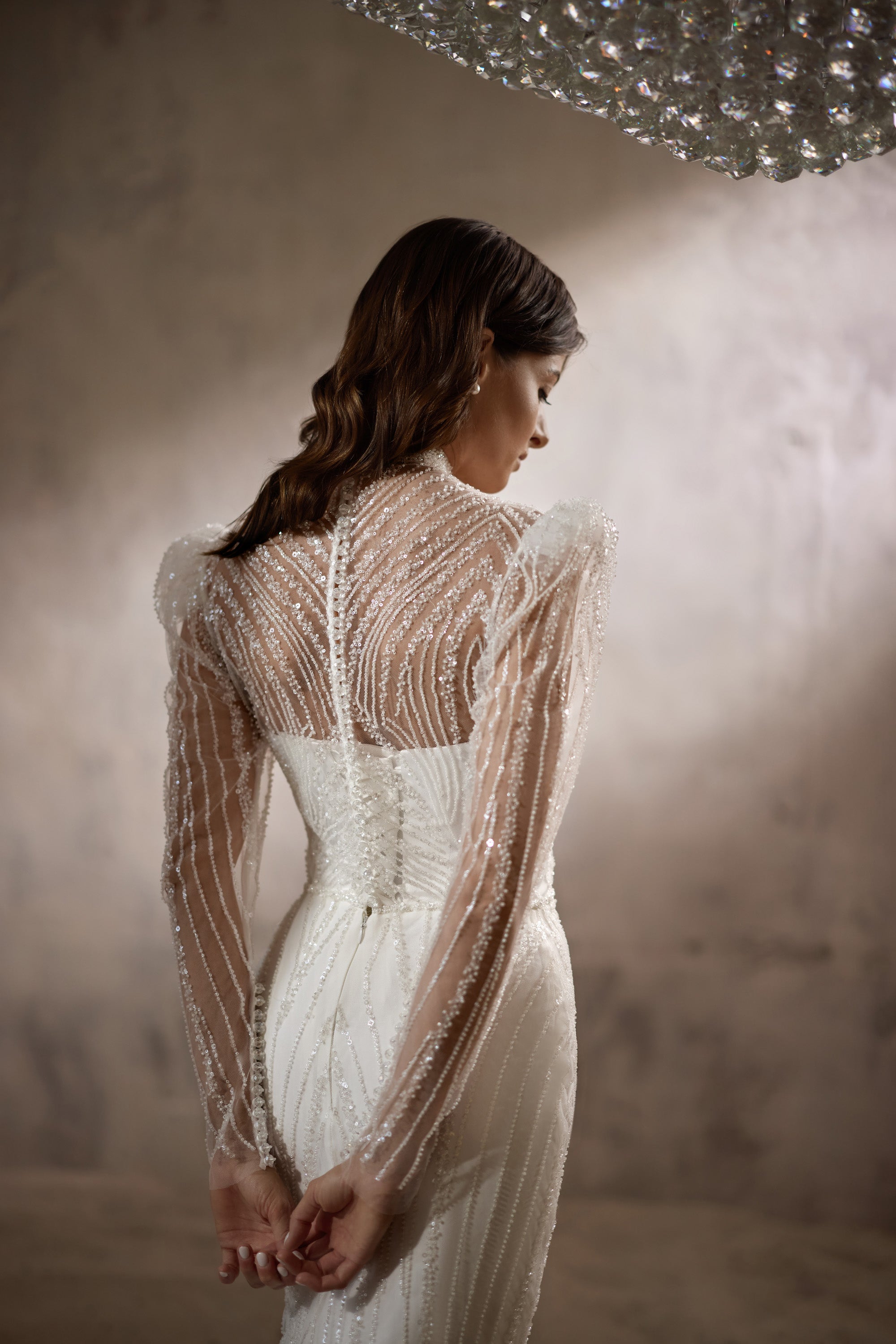 Sheer beaded back and long sleeves on an ivory wedding dress with a fitted sheath silhouette