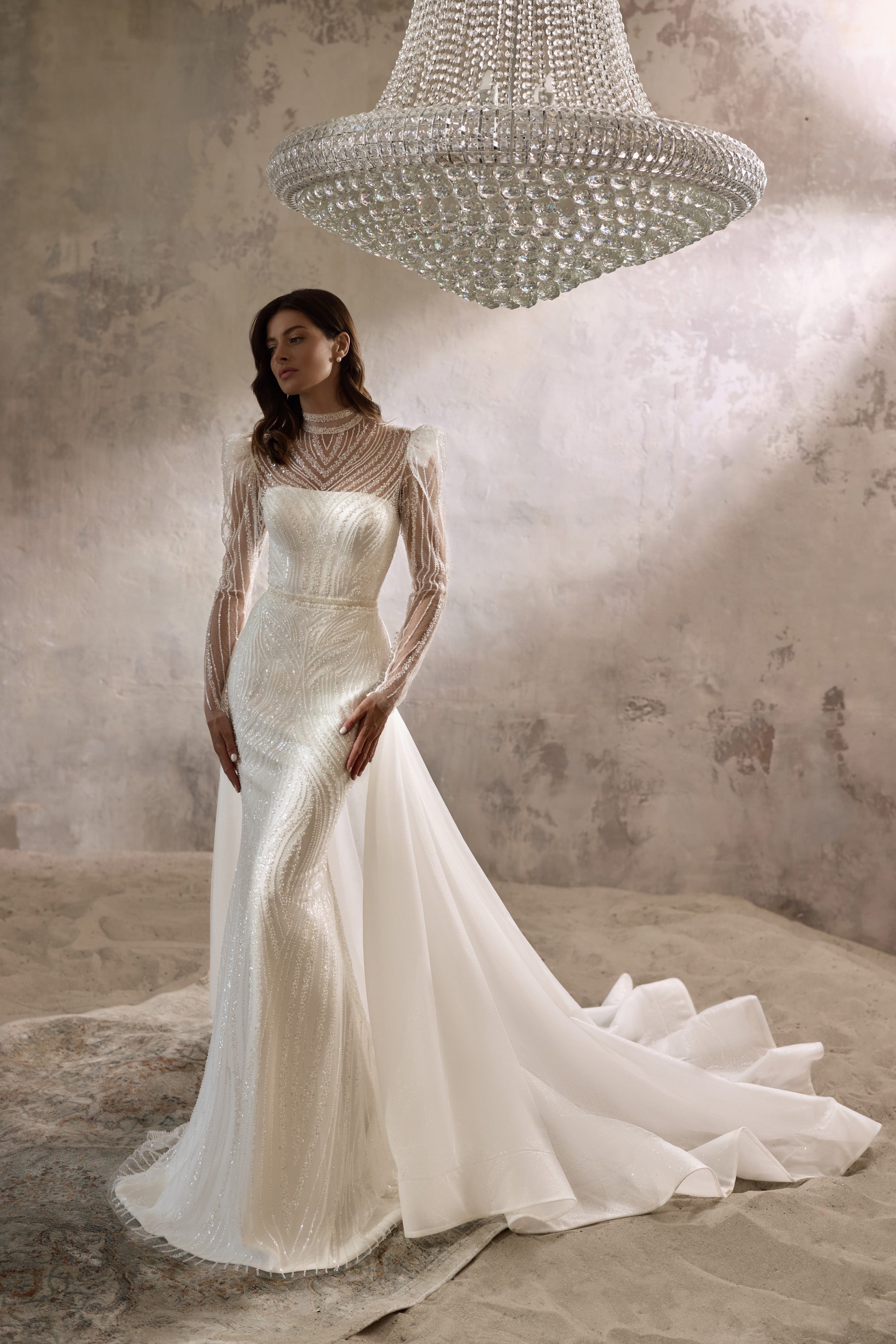 Ivory sheath wedding dress with a high beaded neckline, sheer long sleeves, and flowing overskirt train