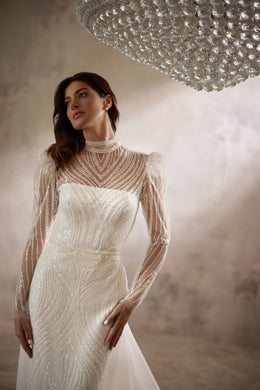 Close-up of an ivory wedding dress with a high beaded neckline, sheer sleeves, and shimmering bodice