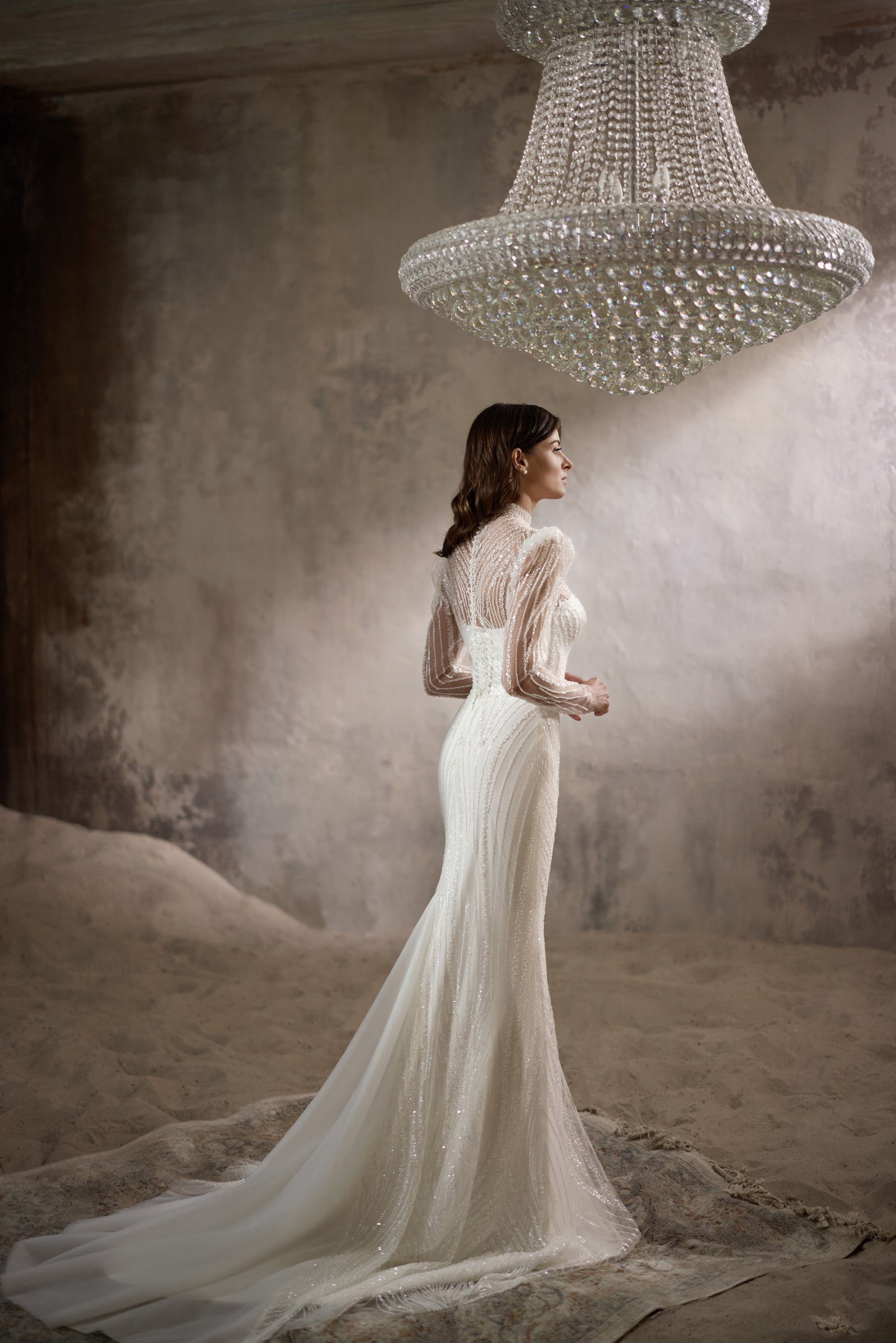 Side view of an ivory sheath wedding dress with sheer beaded sleeves and a long flowing train