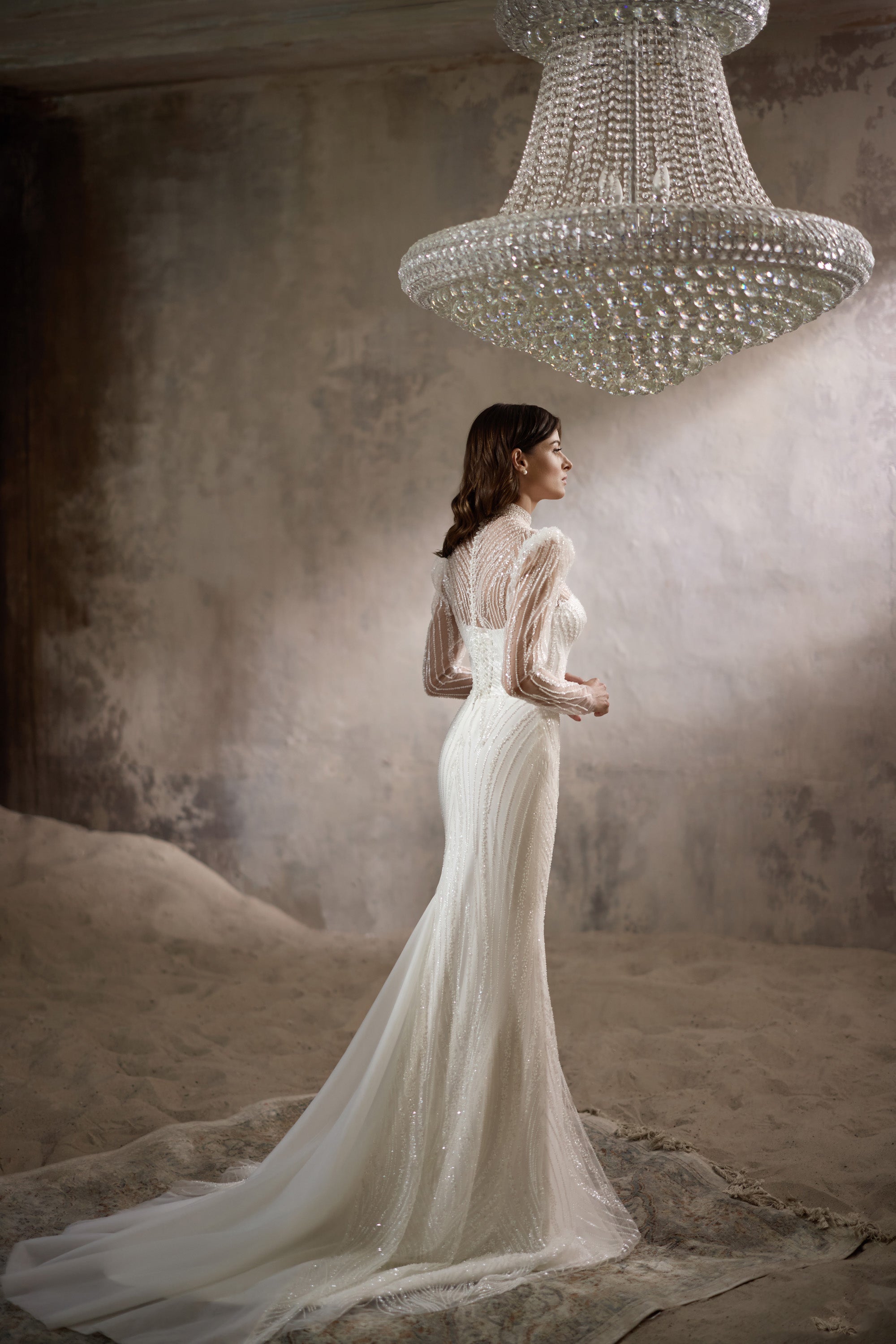 Side view of an ivory sheath wedding dress with sheer beaded sleeves and a long flowing train