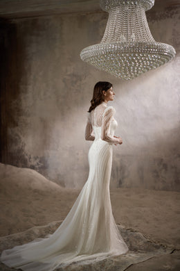 Side view of an ivory sheath wedding dress with sheer beaded sleeves and a long flowing train