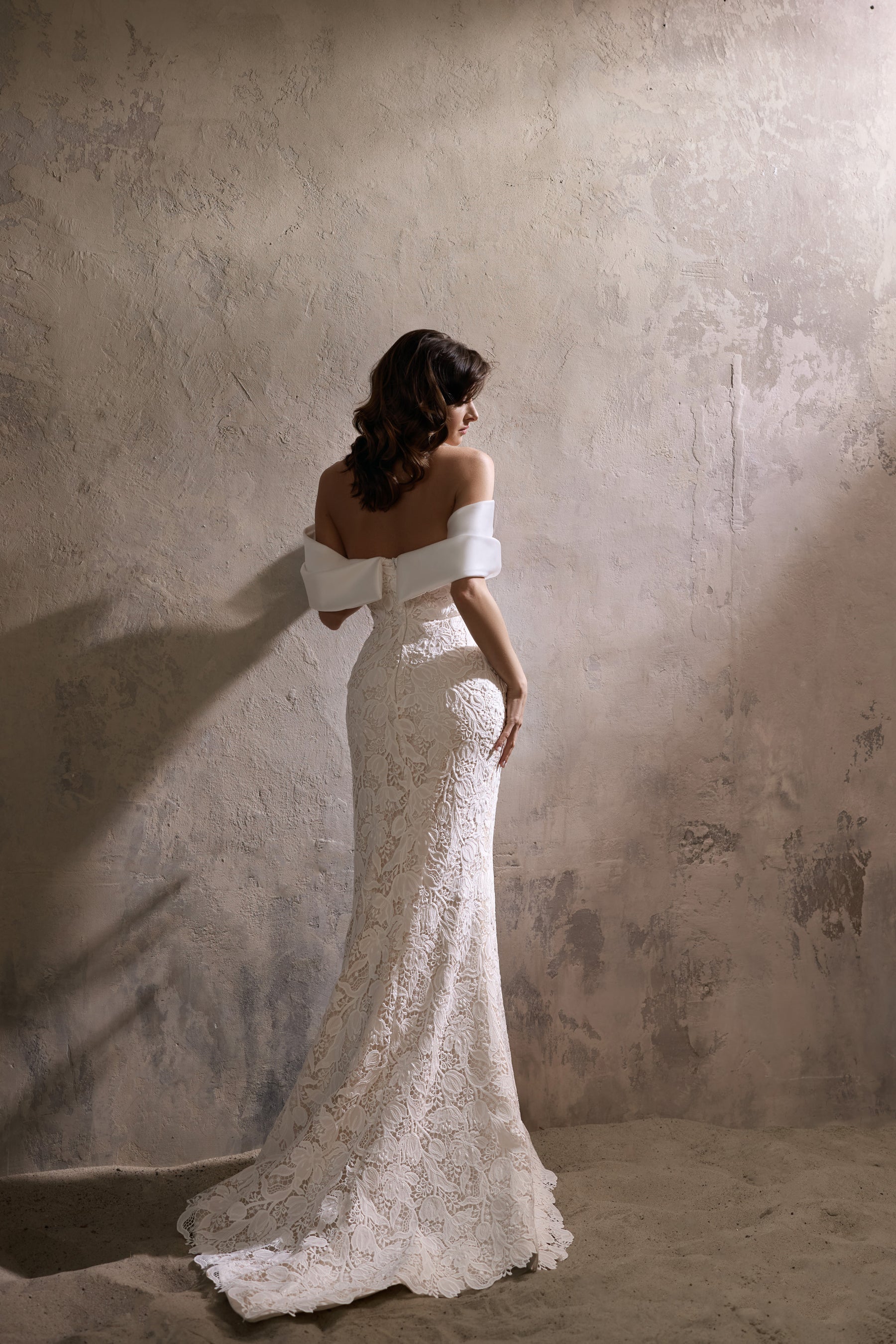 Ivory lace wedding dress showing its off-the-shoulder back, fitted sheath silhouette, and extended train