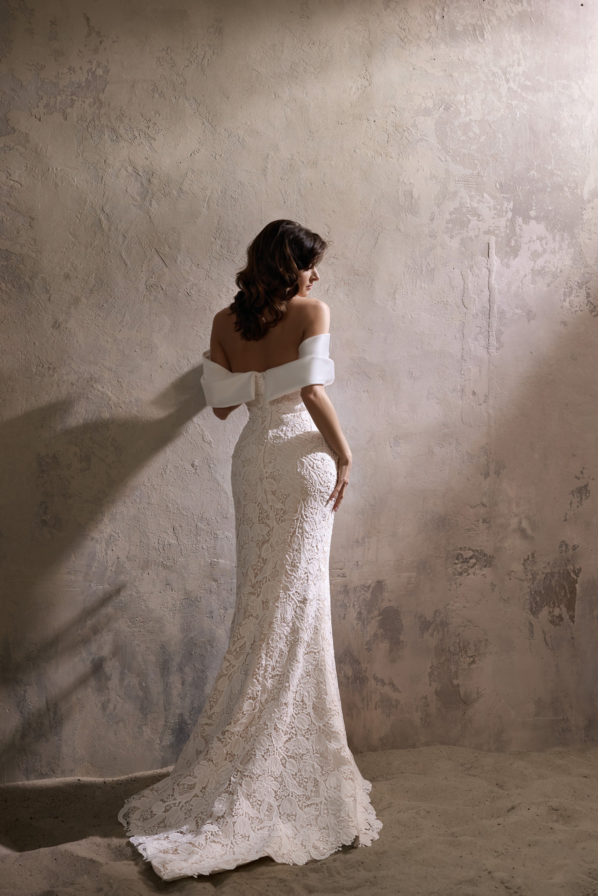 Ivory lace wedding dress showing its off-the-shoulder back, fitted sheath silhouette, and extended train