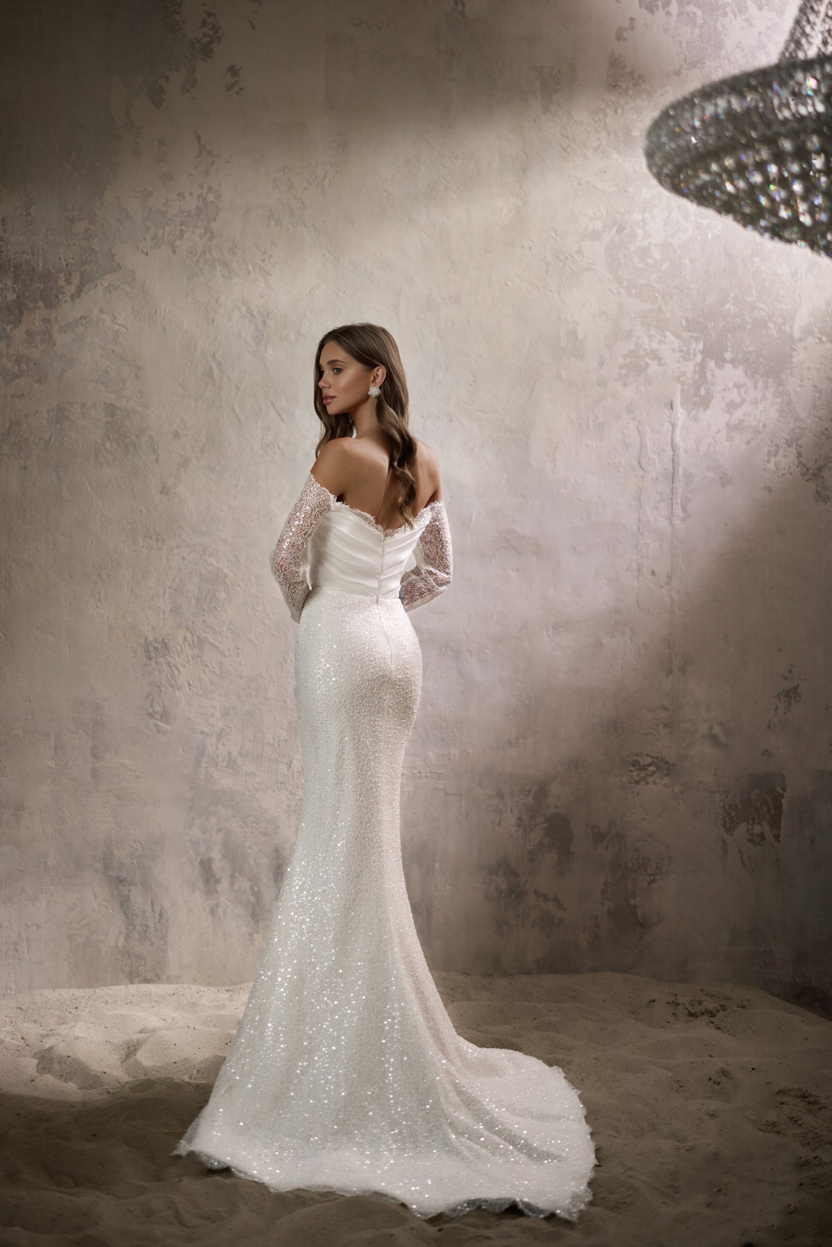 Back view of an ivory mermaid wedding dress with sheer lace sleeves and a sweeping train