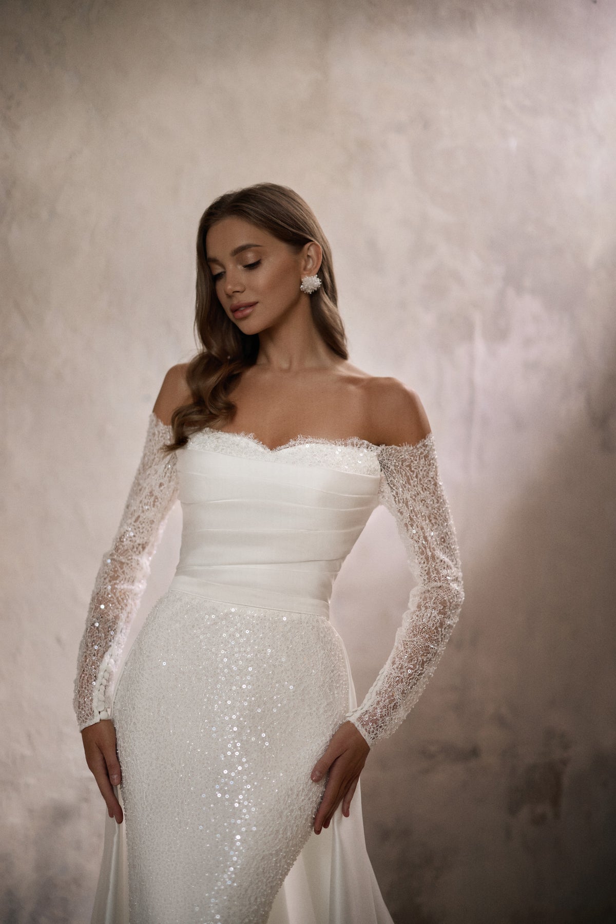 Close-up of an ivory wedding dress with an off-the-shoulder neckline and sparkling lace sleeves