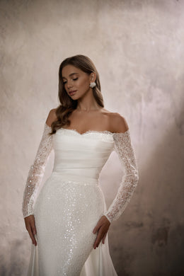 Close-up of an ivory wedding dress with an off-the-shoulder neckline and sparkling lace sleeves