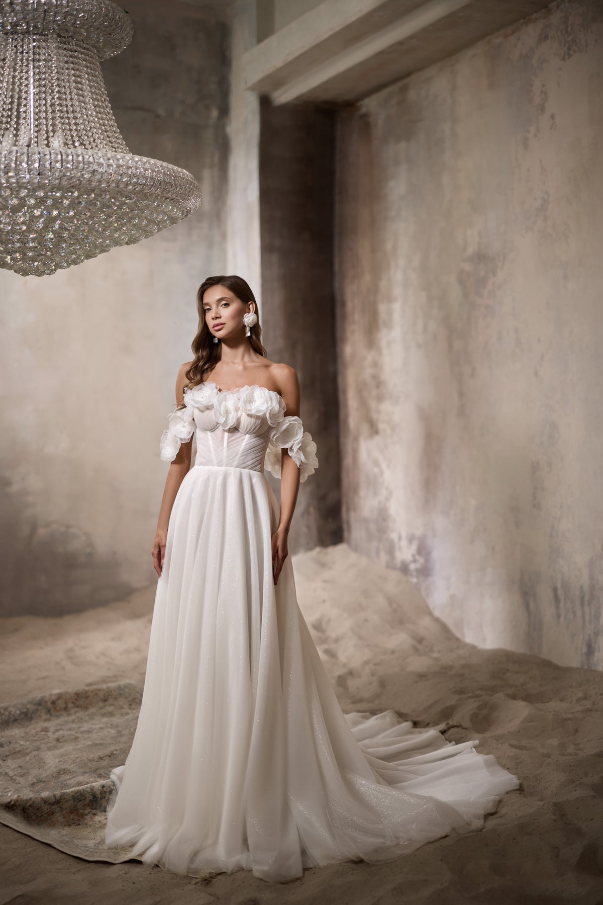 Ivory A-line wedding dress with a fitted bodice, floral off-the-shoulder detail, glittering skirt, and train