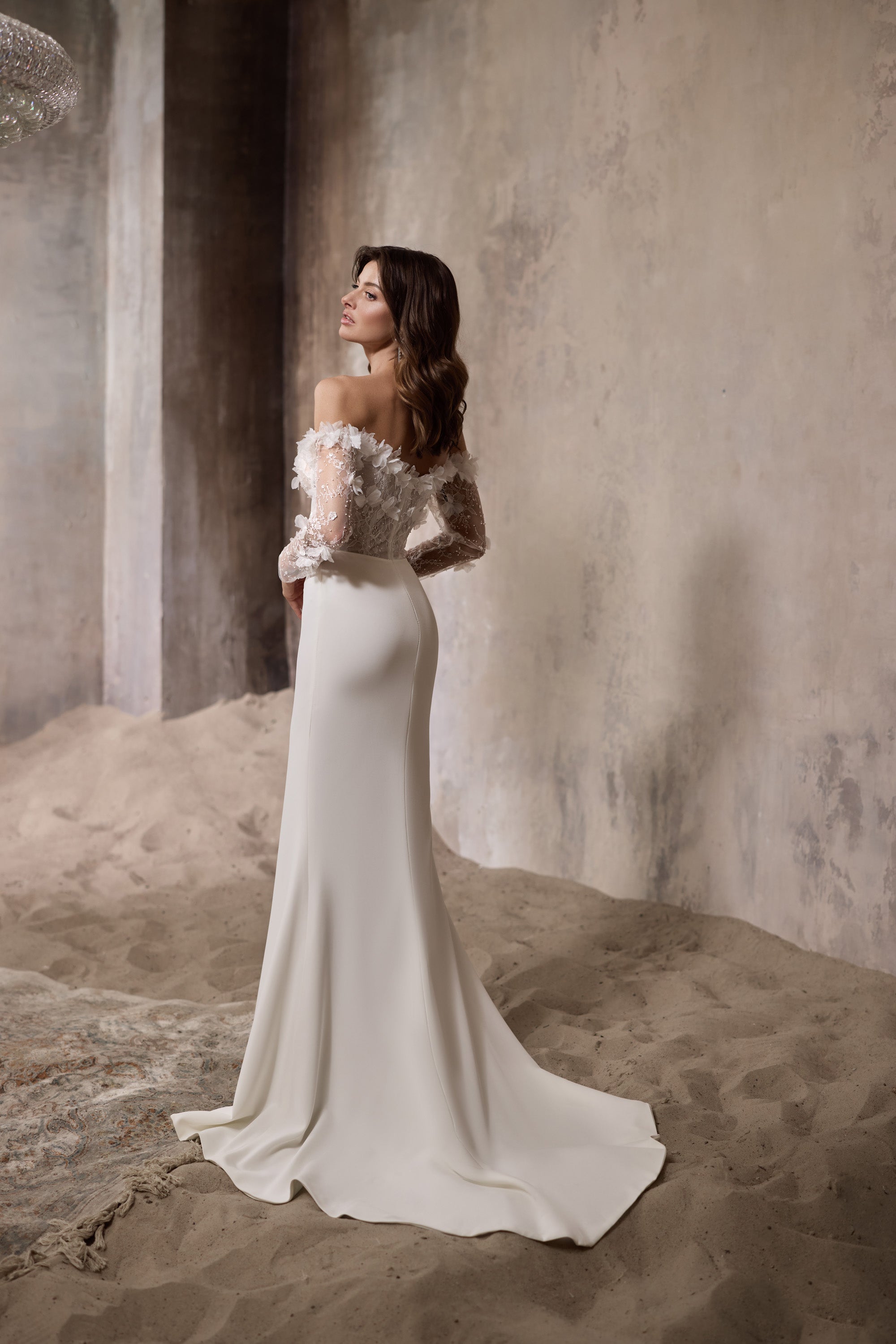 Side profile of an ivory sheath wedding dress with sheer floral sleeves, fitted waist, and trailing hem