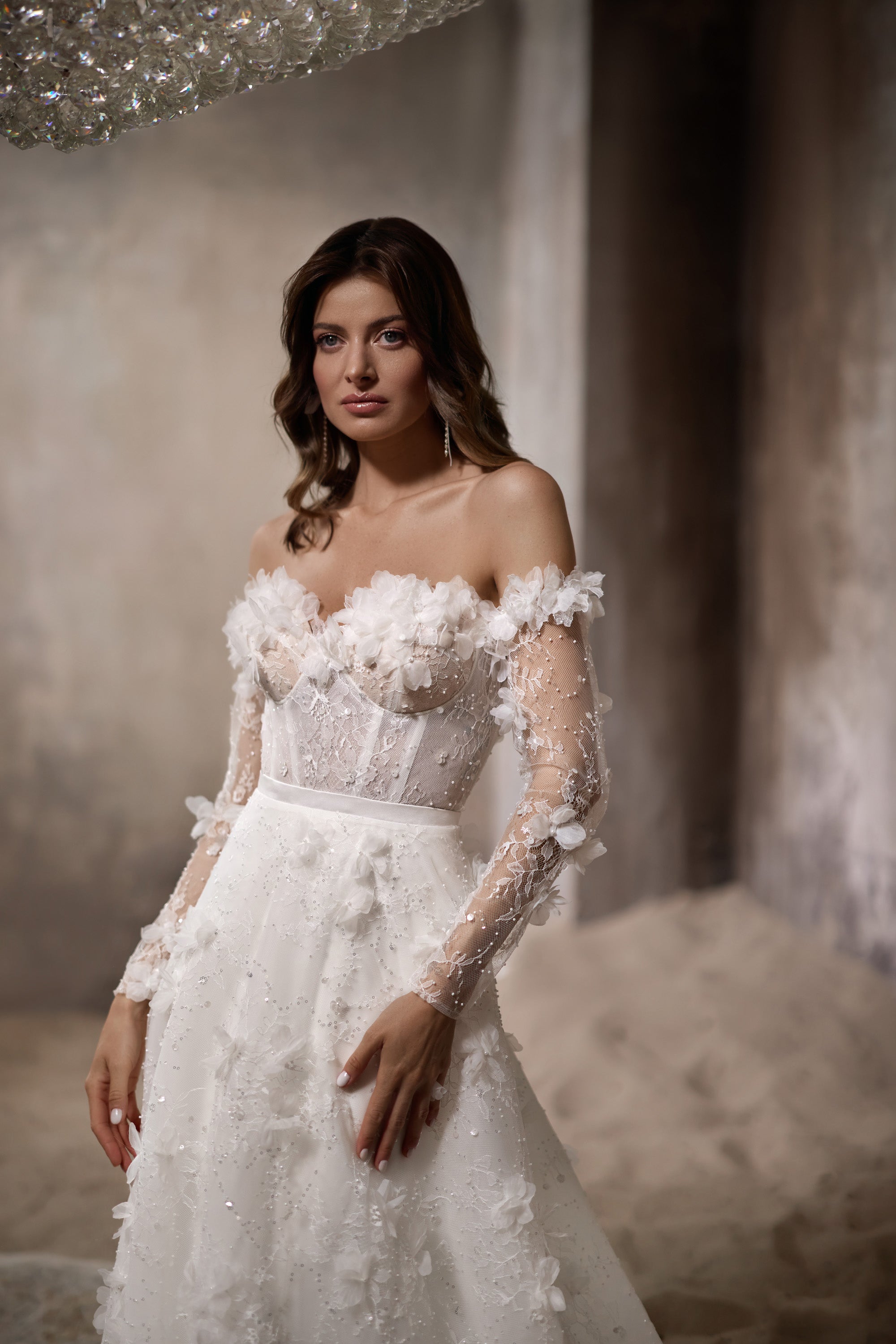 Close-up of an ivory wedding dress bodice with 3D floral appliqués, sheer sleeves, and sparkling beadwork