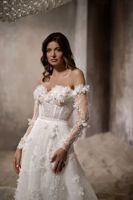 Close-up of an ivory wedding dress bodice with 3D floral appliqués, sheer sleeves, and sparkling beadwork