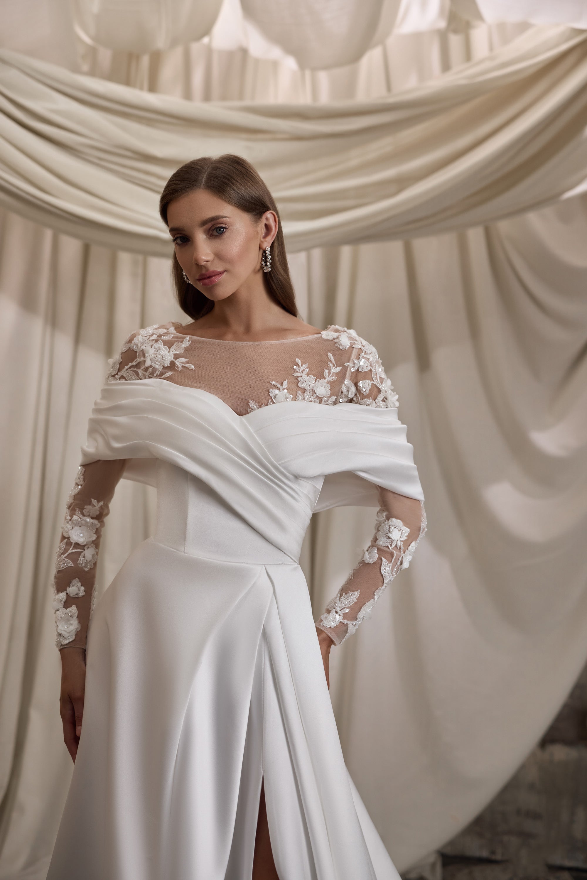 Close-up of an ivory wedding dress with sheer floral lace sleeves and a draped neckline