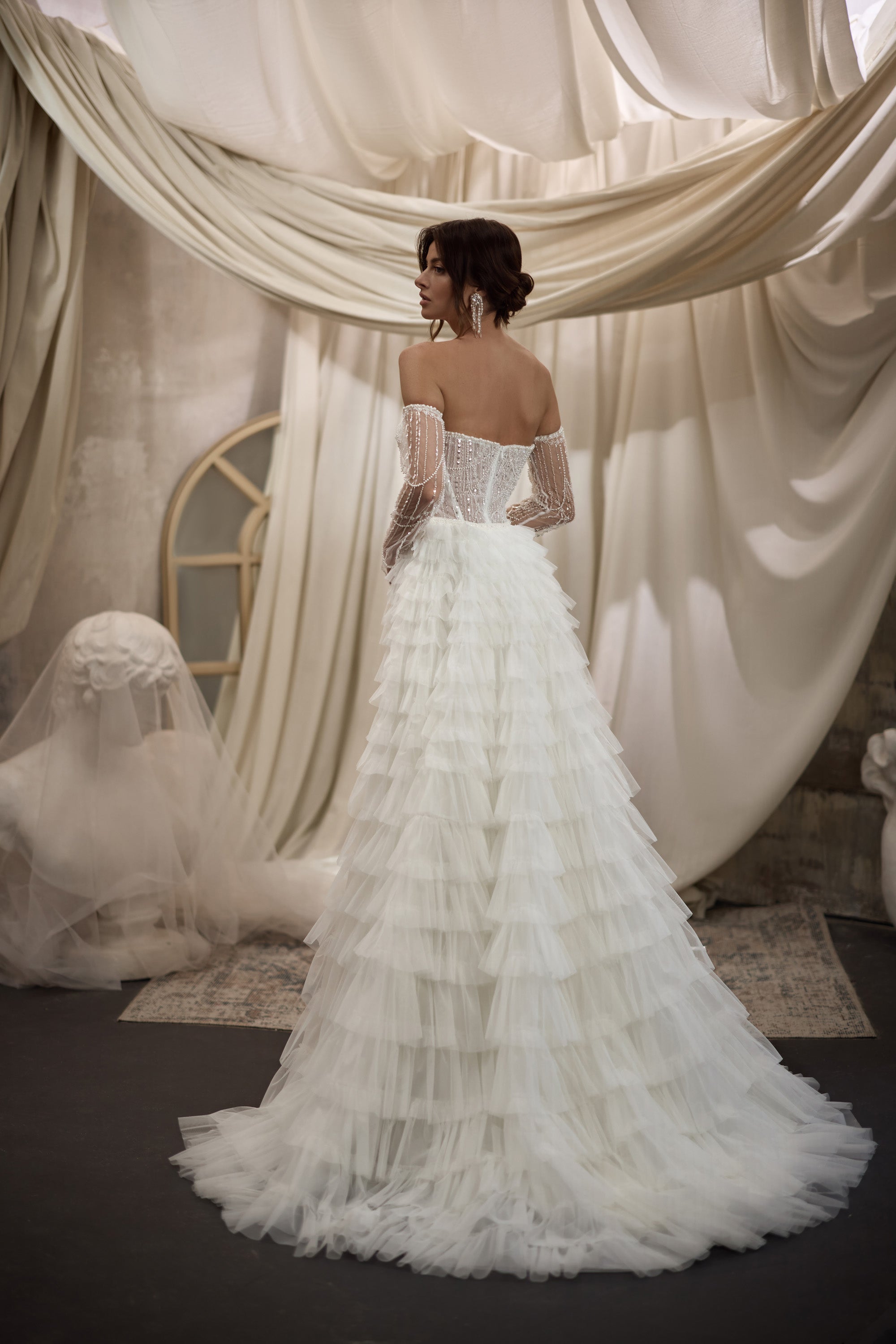 Ivory wedding dress with a sheer beaded back, embellished sleeves, tiered ruffle overskirt, and train