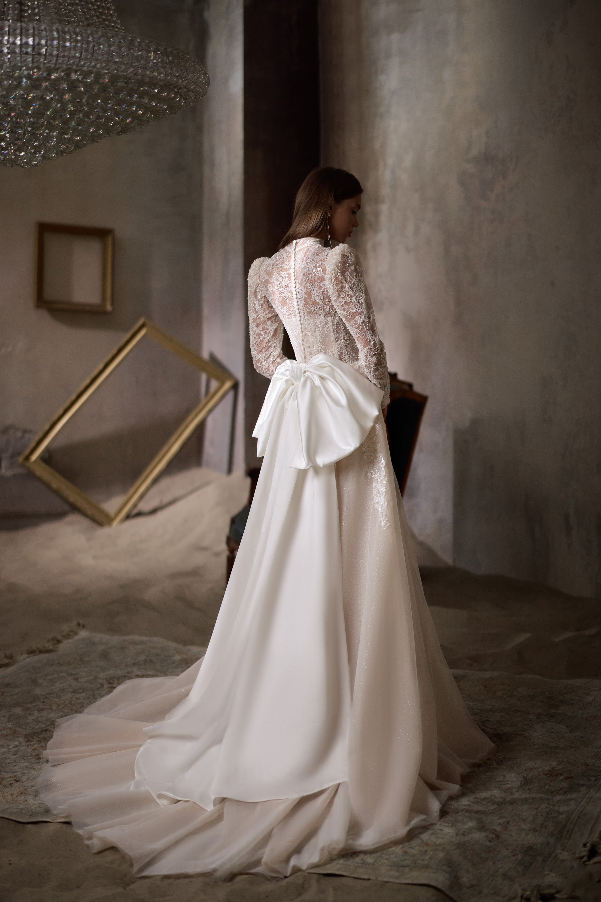Back view of an ivory wedding dress with a large waist bow, long lace sleeves, and a sweeping train