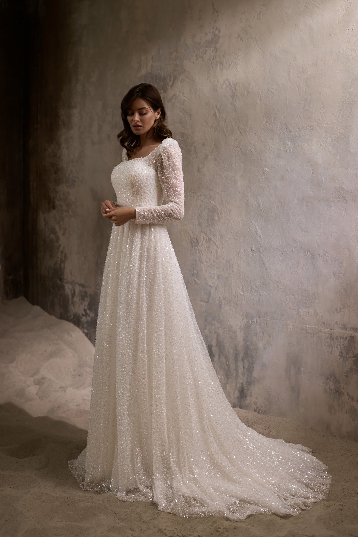 Ivory A-line wedding dress with a square neckline, long sparkly sleeves, and a flowing train