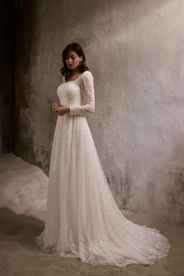 Ivory A-line wedding dress with a square neckline, long sparkly sleeves, and a flowing train