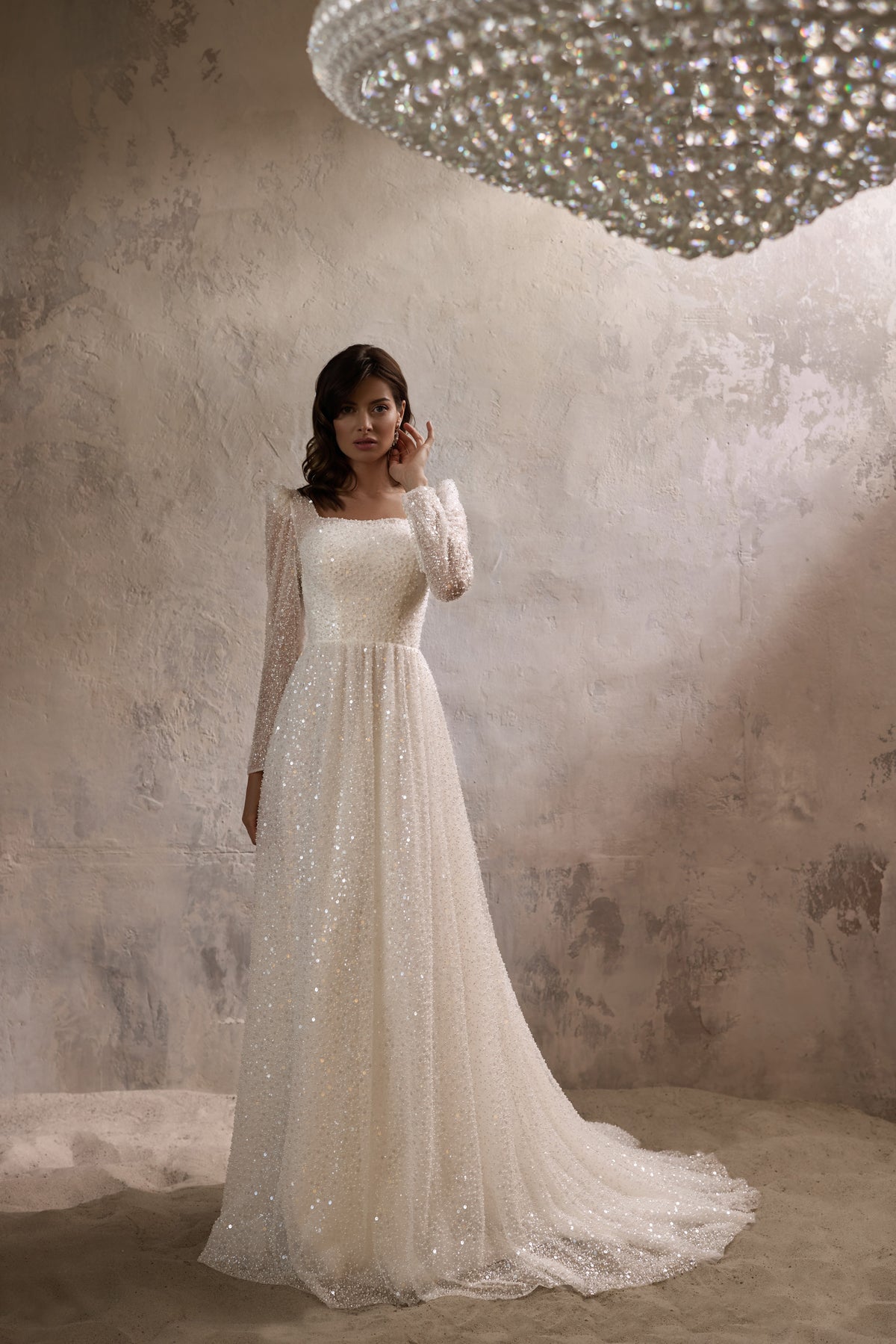 Square-neck ivory wedding dress with long glittering sleeves, an A-line skirt, and a train
